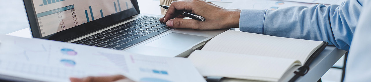 Man in a suit comparing documents in his hands to one on his computer.